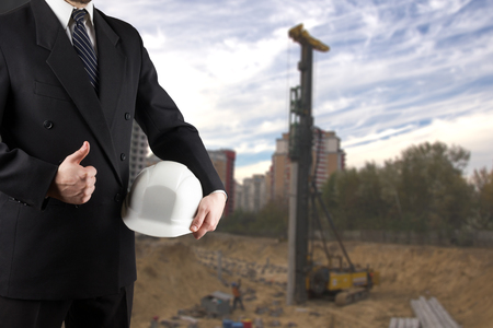 Close up of engineer hand holding white safety helmet for workers security standing in front of  blurred construction site in backgroundの写真素材