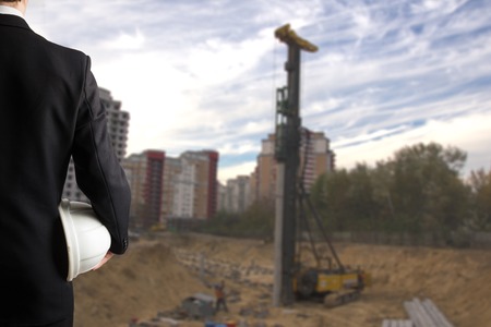 Close up of engineer hand holding white safety helmet for workers security standing in front of  blurred construction site in backgroundの写真素材