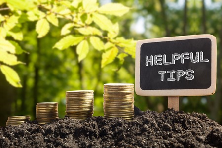 Helpful tips - Financial opportunity concept. Golden coins in soil Chalkboard on blurred urban background.の写真素材