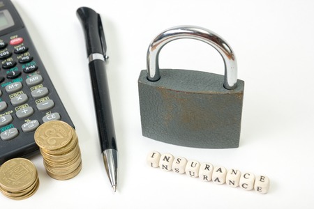 Concept of housing purchase and insurance. Office desk table with supplies top view. Calculator. golden coins, pen, notepad, wooden block with word Insurance.の写真素材