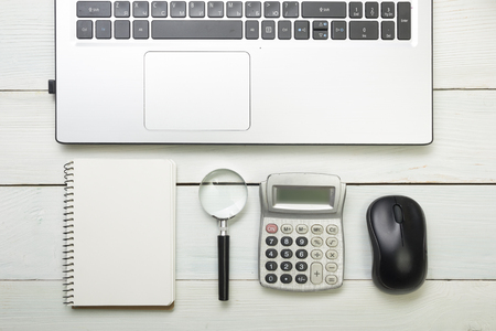 Office desk table with supplies and coffee cup. Top view. Copy space for text. Laptop, notepad, pen, magnifying glass, calculator, remindmer, flowerの写真素材
