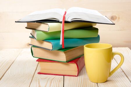 Stack of colorful books, open book and cup on wooden table. Back to school. Copy space.の写真素材