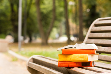 Stack of hardback books and Open book lying on bench at sunset park against blurred nature backdrop. Copy space, back to school. Education backgroundの写真素材