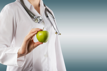 Female doctor's hand holding green apple. Close up shot on grey blurred background. Concept of Healthcare And Medicine. Copy spaceの写真素材