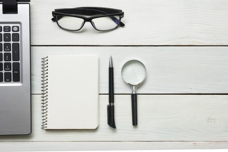 Office desk table with supplies. Top view. Copy space for text. Laptop, blank notepad, pen and magnifying glass.の写真素材