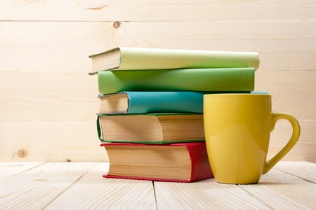 Stack of colorful books and cup on wooden table. Back to school. Copy space.の写真素材