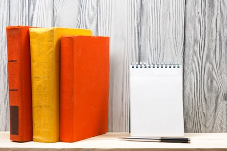 Stack of colorful books, notebook with blank sheet of paper and pen on wooden table. Back to school. Copy space.の写真素材