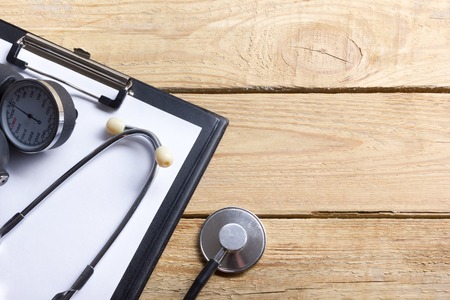Medical clipboard and stethoscope on wooden desk background. Top view. Workplace of a doctorの写真素材
