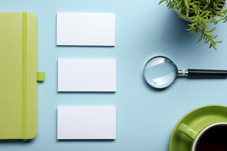 Business card blank, notepad, flower, coffee cup and pen at office desk table top view. Corporate stationery branding mock-up.の写真素材