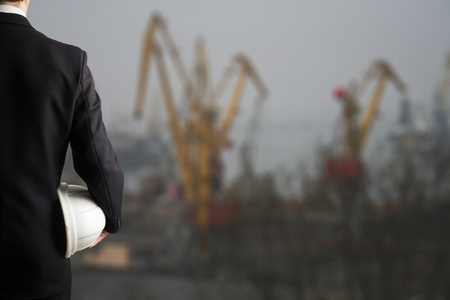 Close up of engineer hand holding white safety helmet for workers security standing in front of urban background.の写真素材