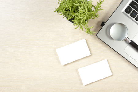 Business card blank, laptop, flower and magnifying glass at office desk table top view. Corporate stationery branding mock-up.の写真素材