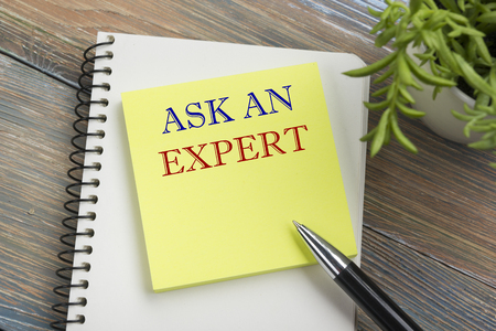 Ask an expert. Notepad with message, pen, reminder and flower. Office supplies on desk table top viewの写真素材