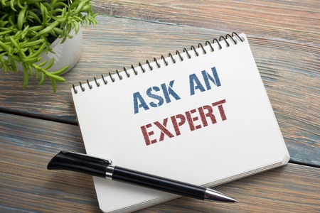Ask an expert. Notepad with message, pen, reminder and flower. Office supplies on desk table top viewの写真素材