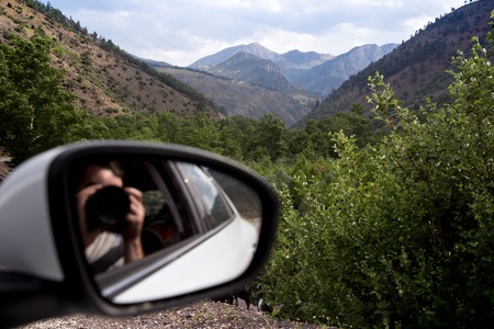 Young woman photographing landscapes near her car on the top of mountainの写真素材