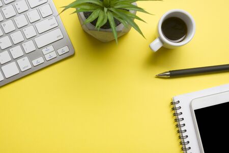 Yellow desk office with laptop, smartphone and other work supplies with cup of coffee. Top view with...