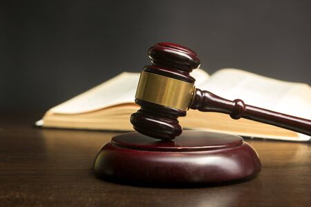 Law concept - Open law book with a wooden judges gavel on table in a courtroom or law enforcement...
