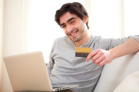 View of a Young relaxed man paying online with credit card in sofaの写真素材