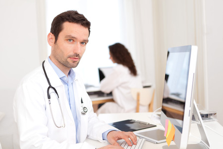 View of a Doctor working at the office with nurse in backgroundの写真素材