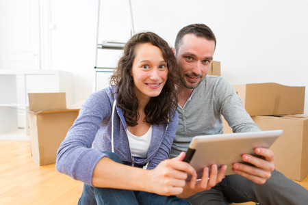 View of a Young couple using tablet while moving in new flatの写真素材