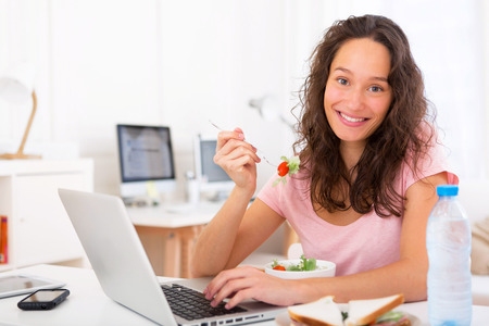 View of a Young attractive student eating salad while workingの写真素材