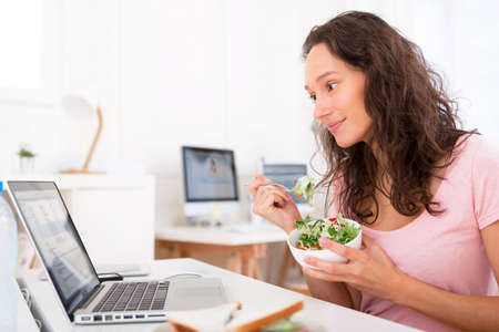 View of a Young attractive student eating salad while workingの写真素材