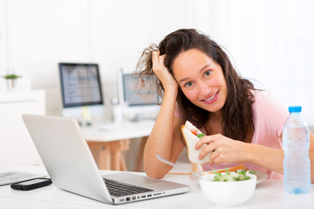 View of a Young attractive student  eating sandwich while workingの写真素材