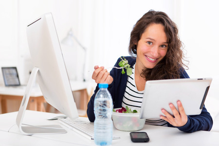 View of a Young attractive student eating salad while using tabletの写真素材