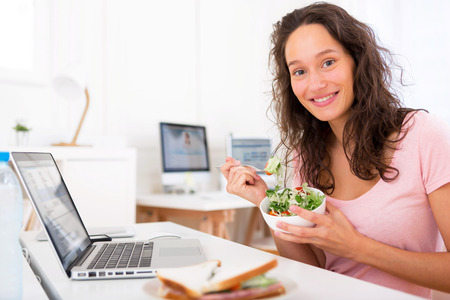 View of a Young attractive student eating salad while workingの写真素材