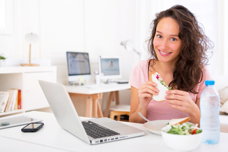 View of a Young attractive student  eating sandwich while workingの写真素材