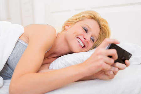 View of a Young attractive woman sending ttext in a bedの写真素材