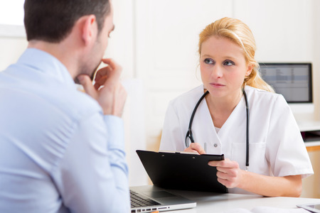 View of a Young attractive doctor taking notes while patient speakingの写真素材