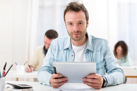 View of a Young attractive student using his tablet during classesの写真素材