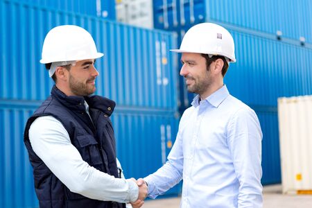 View of a Docker and supervisor handshaking in front of containersの写真素材