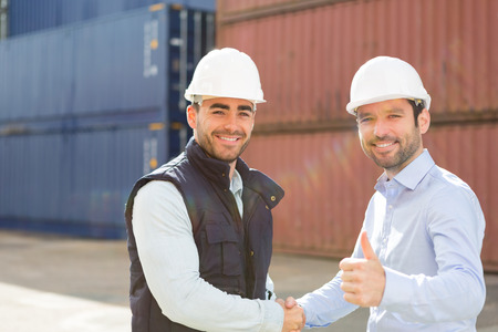 View of a Docker and supervisor handshaking in front of containersの写真素材