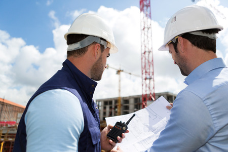 View of a Engineer and worker watching blueprint on construction siteの写真素材