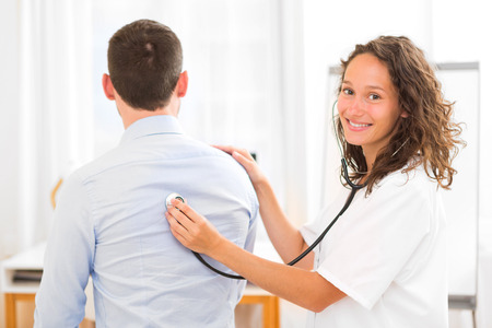 View of a Young attractive doctor checking patient's heart beatmentの写真素材