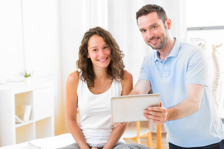 View of a Young attractive physiotherapist using tablet with patientの写真素材