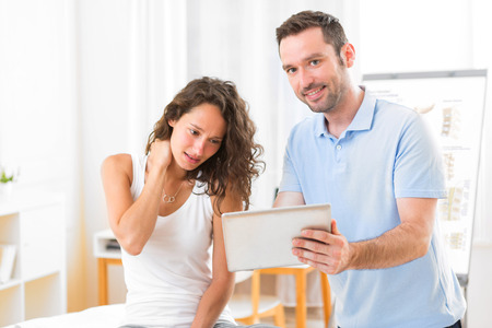 View of a Young attractive physiotherapist using tablet with patientの写真素材