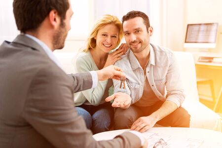 View of a Real estate agent delivers keys of new house to young coupleの写真素材