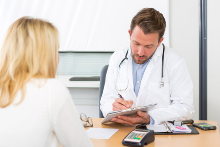 View of Young attractive doctor taking notes while patient speakの写真素材