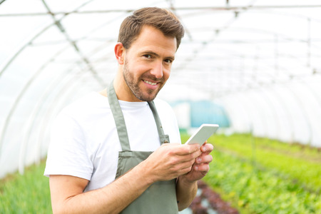 View of an attractive farmer in a greenhouse using mobileの写真素材