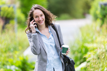 View of a Young attractive business woman walking in the park, with phone and coffeeの写真素材