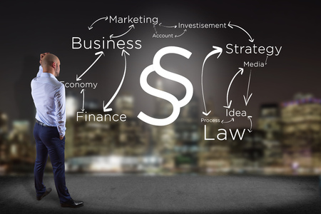 View of a Businessman in front of a wall with Justice and law symbol displayed on a futuristic interface with business terms - technology and inspiration conceptの写真素材