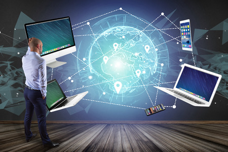 View of a Businessman in front of a wall with Computer and devices displayed on a futuristic...