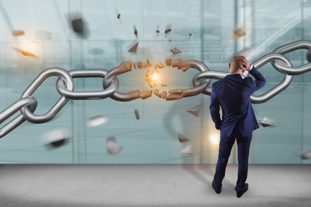 View of a Businessman in front of a wall with Weak link of a Broken chain exploding - 3d render