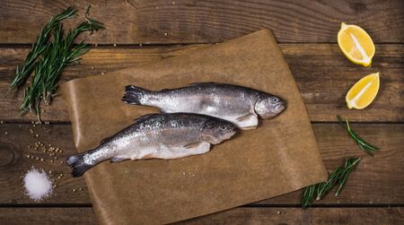trout with spices, herbs and a lemon on a wooden tableの写真素材