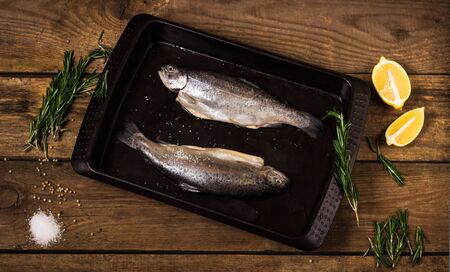 fish with spices, herbs and a lemon on a wooden tableの写真素材