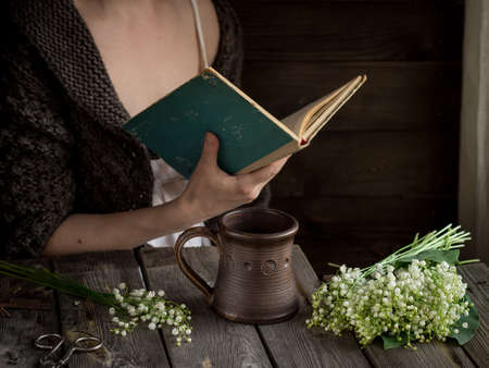 A girl with mug,white flowers and book. Selective focus. Style rustic. Dark tones.の写真素材
