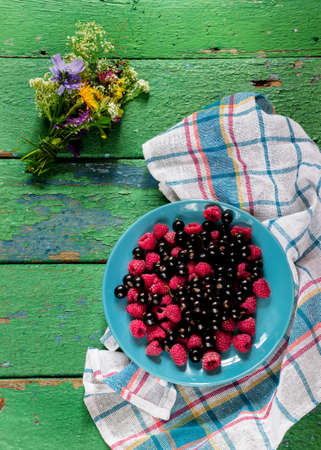 Summer berries on blue plate on old rustic painted cracky green (turqouise) wooden background. Selective focus.の写真素材