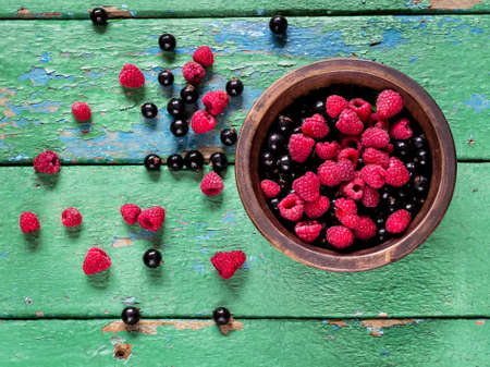 Summer berries in the bowl on old rustic painted cracky green (turqouise) wooden background.